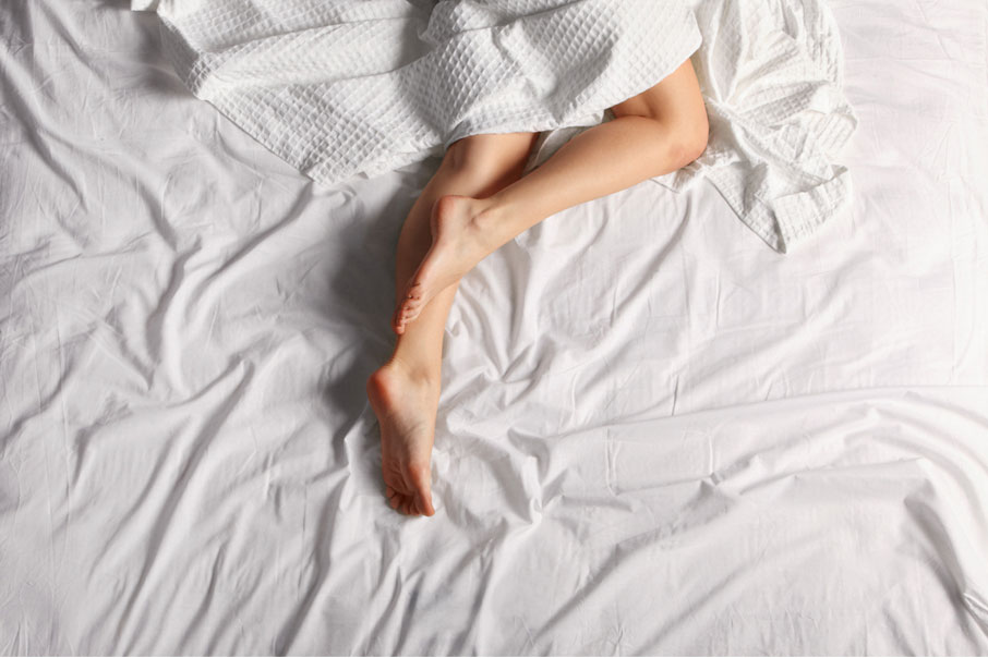 Woman-sleeping-under-white-sheet-legs-exposed-to-cool-off