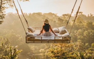Woman on bed swing above tropical forest